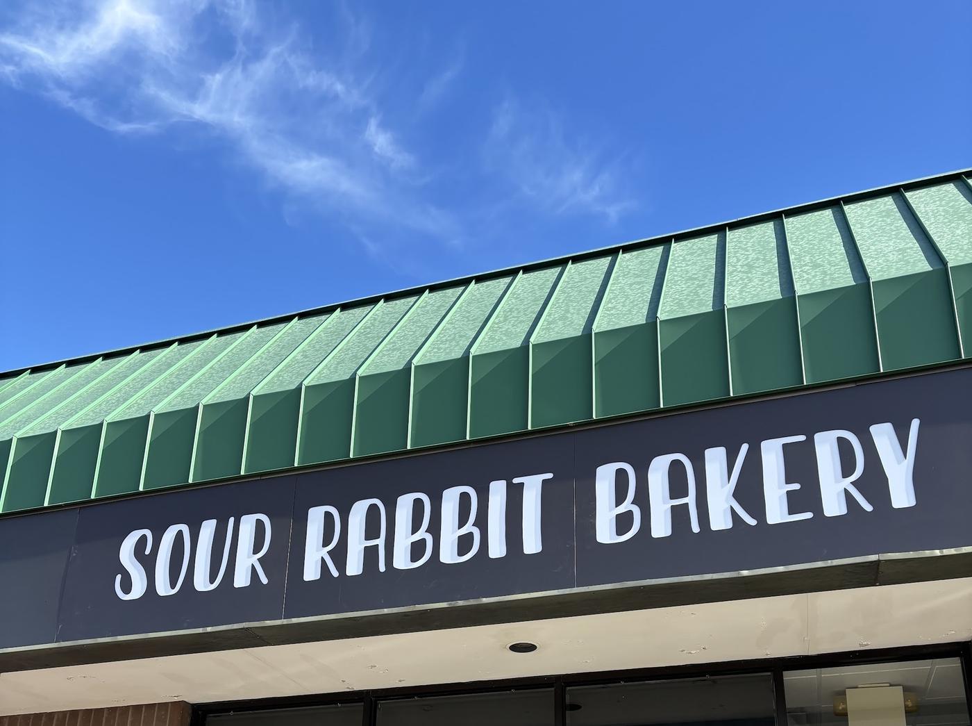 The Sour Rabbit Bakery storefront: a green standing seam awning over a brick front with the bakery's name on the fascia.